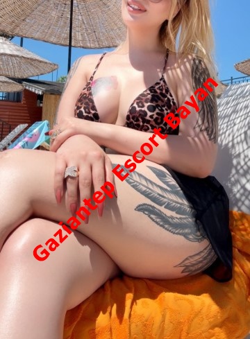 Woman in a leopard-print bikini sits on an orange towel at the beach; bold red text across reads 'Gaziantep Escort Bayan', with visible leg tattoos. Woman in a leopard-print bikini sits on an orange towel at the beach; bold red text across reads 'Gaziantep Escort Bayan', with visible leg tattoos.