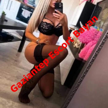 Woman in black lace lingerie posing on her knees in a bedroom, taking a mirror selfie; red text advertises Gaziantep Escort Bayan.