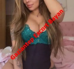 Woman in teal lace bra and black waist cincher posing on a bed in a bedroom; red diagonal overlay reads 'Gaziantep Escort Bayan'.