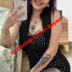 Selfie of a tattooed woman in a black polka-dot outfit, holding a glittery phone case, with red 'Gaziantep Escort Bayan' text across.