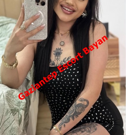 Selfie of a tattooed woman in a black polka-dot outfit, holding a glittery phone case, with red 'Gaziantep Escort Bayan' text across.